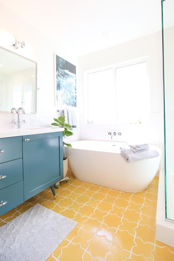 an airy and cheerful bathroom with a yellow tile floor and a teal vanity plus all whites to create a bold look