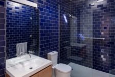 a bathroom clad with deep blue subway tiles, a neutral ceiling and floor and a floating vanity