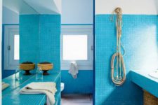 a beach bathroom clad with bright blue tiles, with wicker touches and baskets for a stronger coastal feel