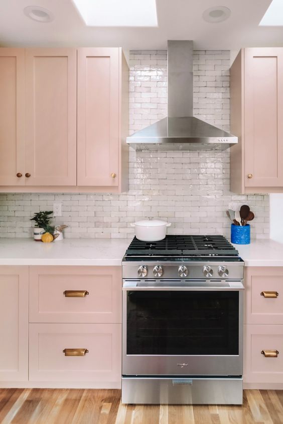 a beautiful blush kitchen with brass handles, a white tile backsplash and skylights is very tender and delicate