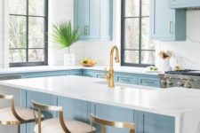 a beautiful light blue kitchen with white marble countertops and a backsplash plus touches of gold and brass