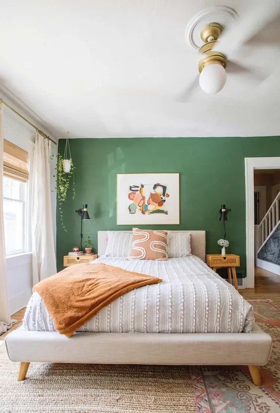 a bedroom with a green accent wall, a neutral upholstered bed and printed bedding, cane nightstands, artwork