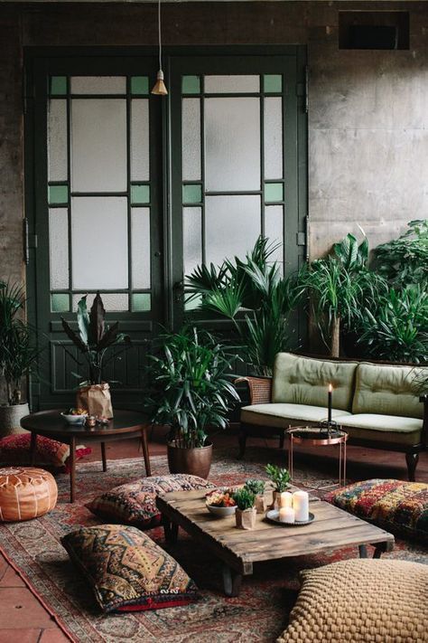 a boho living room with industrial walls, a green loveseat, vintage green doors, potted plants and boho pillows