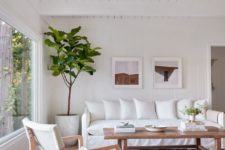 a boho living room with white furniture, a wooden coffee table, a small gallery wall and a tree