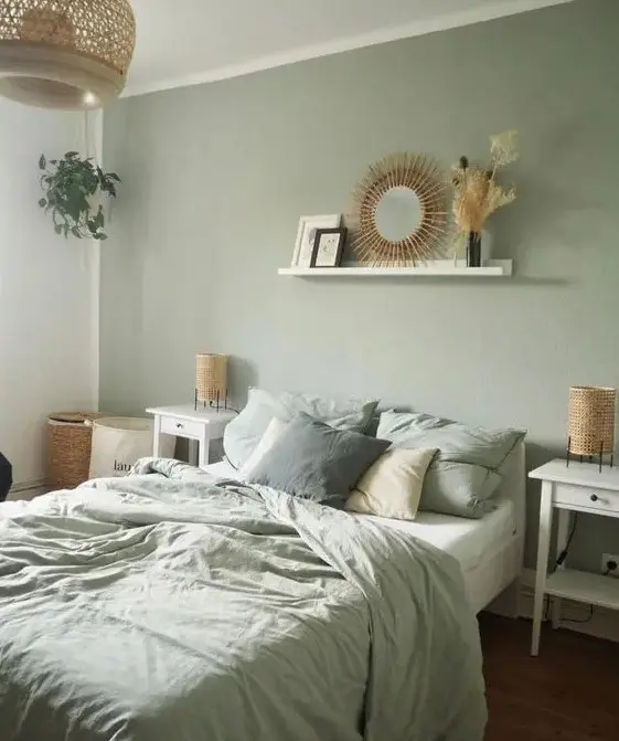 a boho sage green bedroom with white furniture, woven lamps, a ledge with a mirror, a woven pendant lamp and sage green bedding