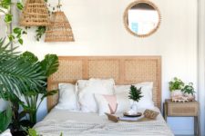 a boho tropical bedroom done in neutrals, a white wooden ceiling, woven pendant lamps and a cool rattan headboard plus lots of greenery