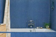 a bold blue tile bathroom with a built-in tub, a wooden vanity and a printed shower curtain