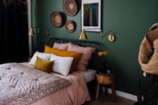 a bold boho bedroom with hunter green walls, a metal bed, a woven pendant lamp and a chic gallery wall