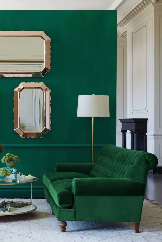a bold living room with an emerald wall, a grene velvet sofa and touches of gold and copper for more chic