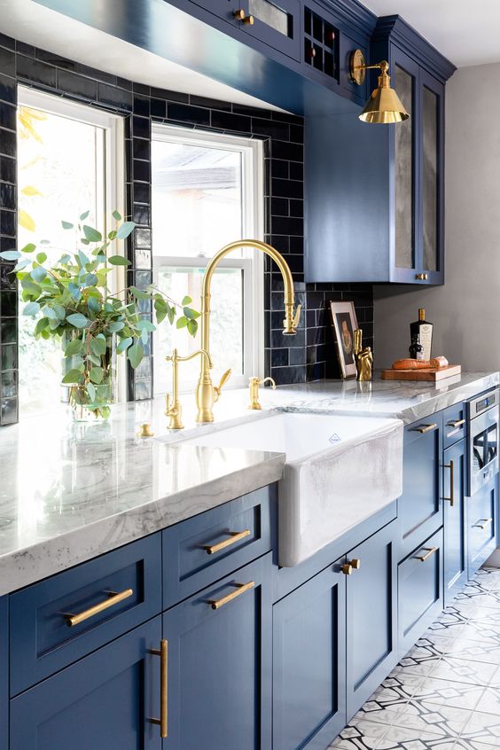 a bright blue kitchen with a black tile backsplash, white stone countertops and touches of gold for more chic