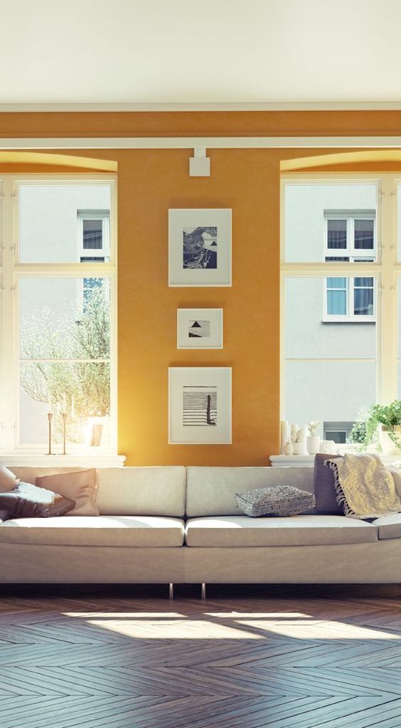a bright contemporary living space with mustard walls, much natural light and artworks between the windows