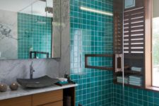 a bright modern bathroom with turquoise tiles, marble walls, a wooden vnaity, a stone sink and a statement mirror