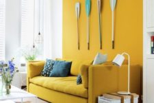 a bright modern living room with a mustard accent wall and a matching sofa, pendant lamps and oars on the wall
