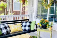 a bright summer porch with a black hanging bench, a vintage table, a candle lantern and lots of colorful blooms