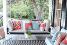 a bright summer porch with a hanging bench, white and mint furniture, colorful pillows and a printed rug