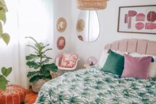 a bright tropical-infused bedroom with a pink bed, a wicker lamp, printed bedding, potted tropical plants