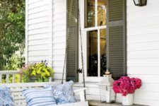 a bright vintage-inspired front porch with a hanging white bench, colorful pillows, a bench, a basket and lots of blooms