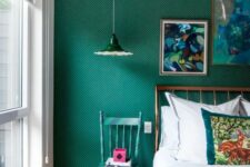 a catchy bedroom with emerald textured walls, a brass bed with neutral bedding, a green and navy chair, a pendant lamp
