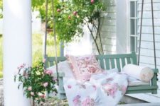 a charming vintage summer porch with a mint hanging daybed with floral bedding, a rose in a pot and more flowers around