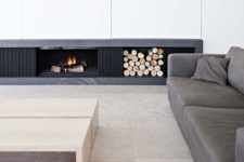 a chic minimalist living room with a built-in fireplace and firewood storage, a grey sofa and neutral tables