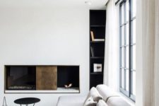 a chic minimalist living room with a white wall with a fireplace, a grey sectional, black furniture and a glazed wall