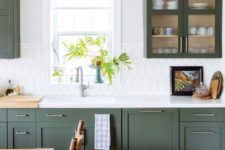 a chic modern farmhouse kitchen in dark green, with a catchy white tile backsplash and touches of brass