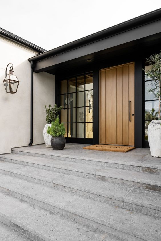 a chic modern farmhouse porch with potted plants, glazed walls and a stained heavy door looks very elegant and chic
