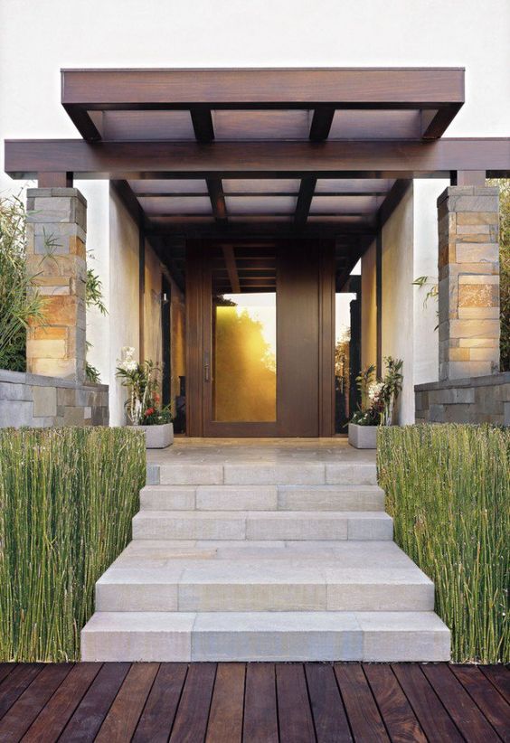 a chic modern front porch with ambmoo on both sides of the staircase, potted plants and blooms and a dark-stained door