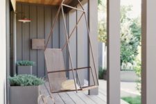 a chic modern porch clad with wood, with pillars, grey metal planters with greenery and a metal suspended chair