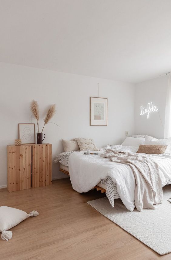 a chic neutral bedroom with a large bed, a wooden cabinet, a neon light and an artwork plus some textiles