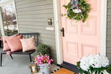 a chic summer porch with a black bench, pink pillows, a greenery wreath, lots of blooms and a chalkboard sign