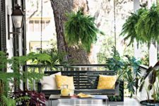 a chic summer porch with a black hanging bench, a black table and black planters with lots of greenery around