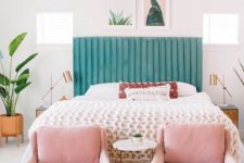 a chic tropical bedroom with a green upholstered bed, pink chairs, cacti and succulent artworks and tropical plants