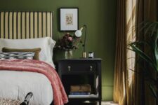 a chic vintage bedroom with green walls, a striped upholstered bed, printed bedding, a black nightstand and some decor