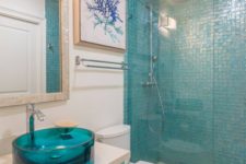 a coastal turquoise bathroom with white walls, turquoise tiles in the shower, a turquoise vanity and a blue sink