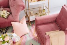 a colorful living room with pink furniture, blush pillows, a bright printed rug and touches of gold