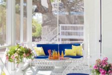 a colorful summer screened porch with modern white furniture, bright upholstery, colorful pillows and blooms