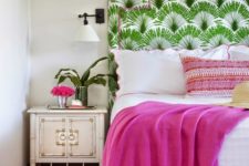 a colorful tropical bedroom with a printed bed, fuchsia textiles, a vintage nightstand and some blooms