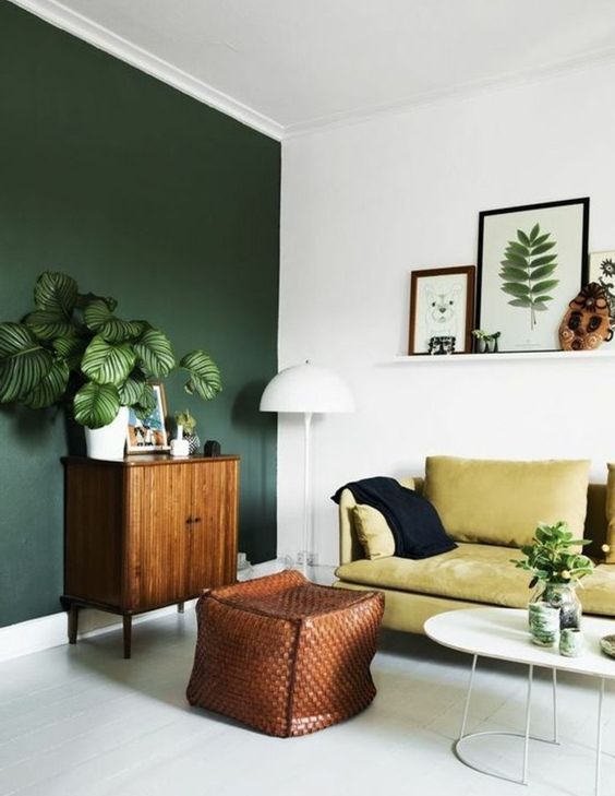 a contrasting living room with a hunter green accent wall, a mustard sofa, a wooden cabinet and a leather woven ottoman