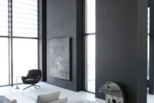a contrasting minimalist space with black accent walls, several windows, a grey sectional and dark tables