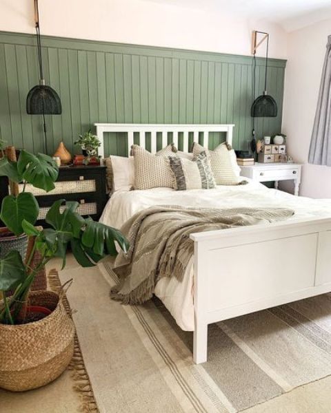 a cool bedroom with a green planked accent wall, a white bed with neutral bedding, black sconces and a potted plant