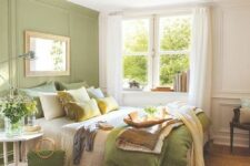 a cozy bedroom with a light green accent wall, a bed with neutral bedding, a nightstand and a dark-stained chair