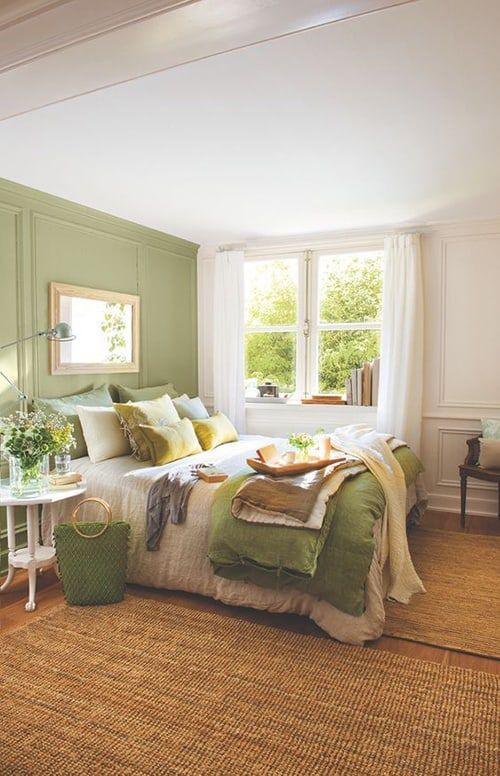 a cozy bedroom with a light green accent wall, a bed with neutral bedding, a nightstand and a dark-stained chair