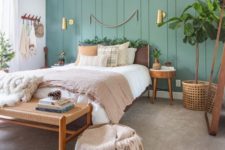 a cozy boho bedroom with a light grene accent wall, some cozy wood and rattan furniture and potted greenery
