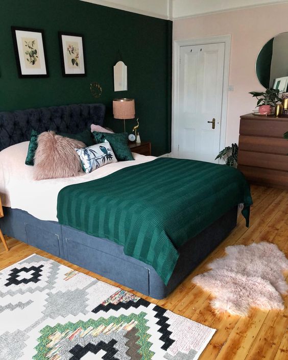 a cozy room with pink walls and a hunter green accent one, with hunter green bedding and floral artworks