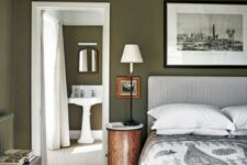 a dark green bedroom with a white fluted headboard bed, stained vintage furniture, artwork and printed bedding