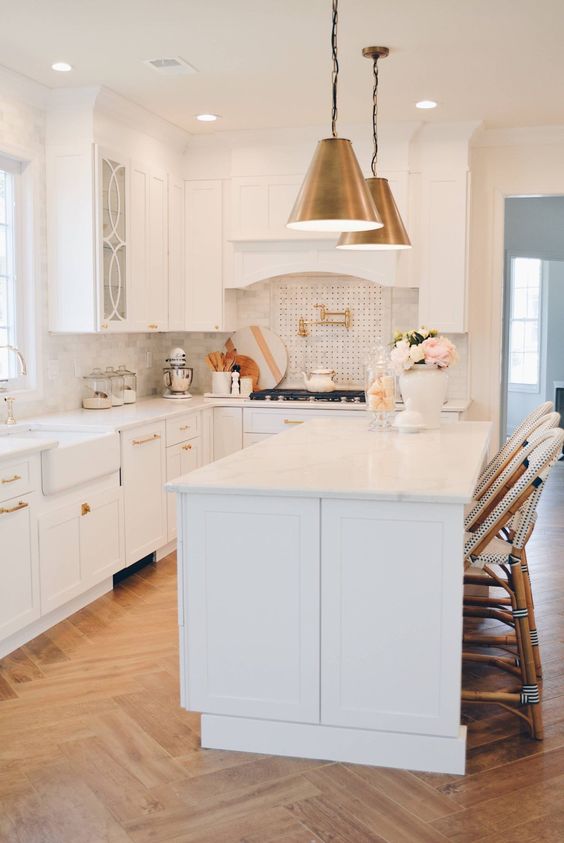 a glam white kitchen with stylish cabinets, a white marble tile backsplash and touches of brass and gold here and there