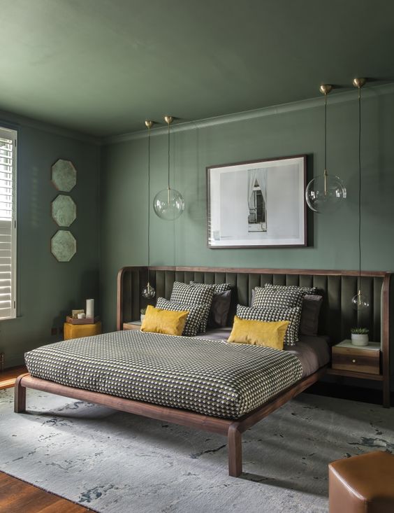 a green bedroom with a bed with an extended headboard and printed bedding, pendant lamps and some art