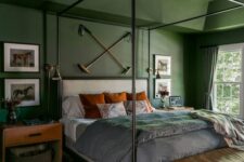 a green bedroom with a black metal canopy bed and bright bedding, stained nightstands, an amber leather bench, a printed rug