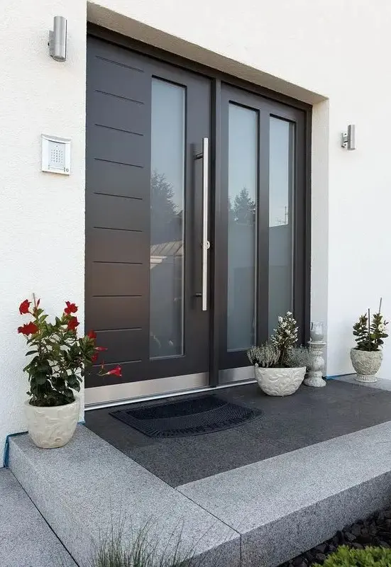a large modern black door with glass inserts, three planters with blooms and greenery on the porch